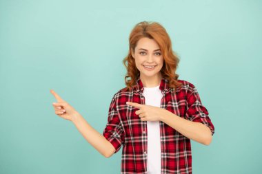 Mavi arka planda damalı tişörtlü mutlu kızıl kadın işaret parmağı.