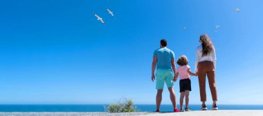 Banner of family embracing on sea beach. Summer family vacation, horizontal banner. Holiday travel background. Mother father and boy looking in future holding hands in summer, back view