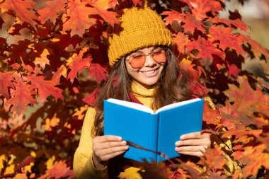 Autumn teenager girl portrait in fall autumn leaves. smiling child hold book on autumn leaves background.