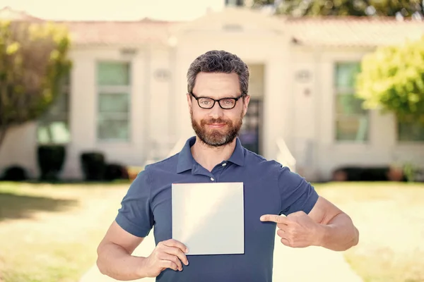 smiling man nerd pointing finger on paper sheet presenting advertisement, copy space, promotion.