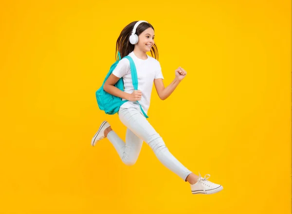 Happy teenager portrait. School teenager child girl in headphones with school backpack. Teenager student, isolated background. Learning music. Jump and run, jumping child