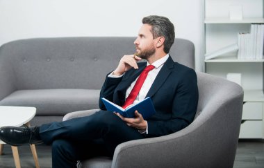 Takım elbiseli olgun iş adamı ofiste oturup not defterine not alıyor..