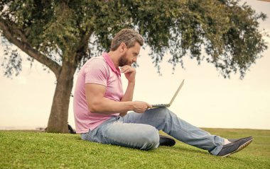 Meşgul adam bilgisayardaki e- postaları kontrol ediyor çimlerde rahatlıyor, online eğitim alıyor..