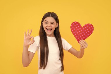 Göz kırpan çocuk, sevgi dolu kalbini göster. Tamam, sarı arka planda jest, 14 Şubat..