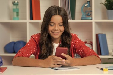 Mutlu çocuk. Uzun kıvırcık saçlı. Sınıfta akıllı telefondan mesaj atıyor..