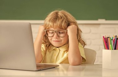 Gözlüklü uykulu çocuk okulda bilgisayar ve eğitimle online ders çalışıyor..