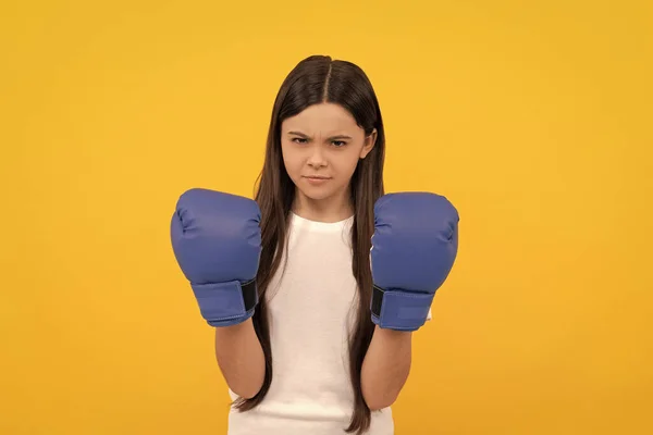 aggressive child in boxing gloves on yellow background.