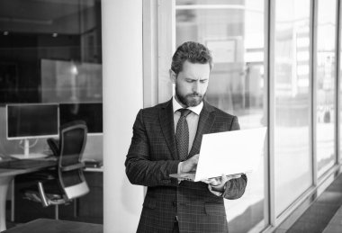 Takım elbiseli sakallı olgun bir adam iş yerinde dizüstü bilgisayar kullanıyor, çevik iş yapıyor..