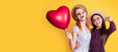 Anne ve kız çocuk afişi, kopyalama alanı, izole bir arka plan. Anne ve kızı gülümsüyor. Sarı arka planda aşk balonu tutuyorlar.