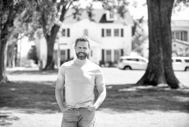 Evin arka planında duran mutlu sakallı adam..