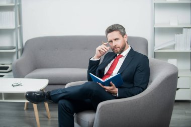 pondering mature businessman in suit sit in office making notes in notebook.