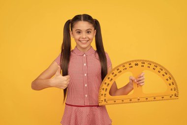 Happy child hold school math tool exractor cetvel üzerinde sarı arkaplan başparmağını göster, cebir.