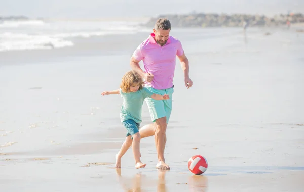 father and son play football on beach. daddy with kid boy on good day. weekend family day. dad and child having fun outdoors. childhood and parenting. family holidays. sport activity.