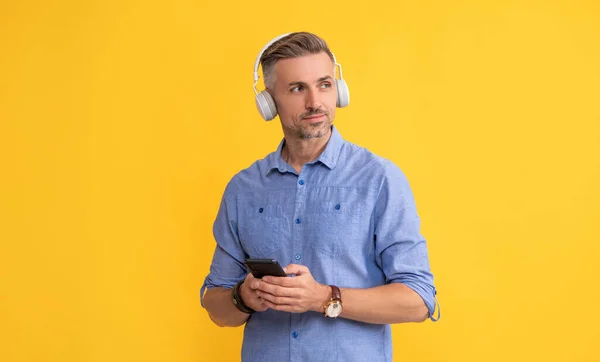new app. guy in headphones chatting on smartphone. man listen music and hold phone. modern life and lifestyle. guy chatting in earphones. musical playlist. mobile music application.