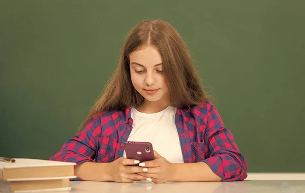 在高中的黑板上忙着在手机上打字的少女 — 图库照片