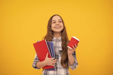 Sarı arka planda kahve fincanı ve not defteri tutan kareli tişörtlü mutlu genç kız, eğitim..