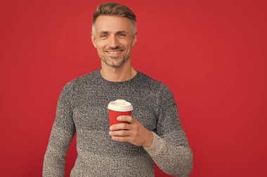 Mutlu adam kırmızı arka planda fincandan kahve içiyor..