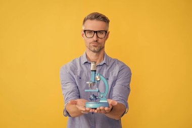 Sarı arka planda mikroskop gösteren gözlüklü olgun bir adam, veri bilimi.