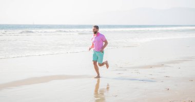 Yalınayak koşucu. Spor atleti deniz gündüz yarışını kazanmak için hızlı koşar. Sabah sporu aktivitesi. Güneşli sahilde koşan sağlıklı bir adam. Enerjik bir yaz. Koşucu özgürlüğü hisseder. Acele et. Dayanıklılık ve dayanıklılık.