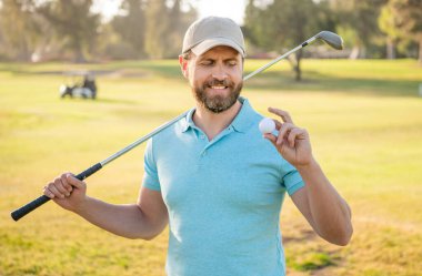 Yaz etkinliği. Profesyonel açık hava sporu. Golf topunu gösteriyor. Profesyonel golf sahasında erkek golfçü. Golf sopasıyla şapkalı golfçünün portresi. İnsanların yaşam tarzı. Yeşil çimlerde adam üstüne adam.
