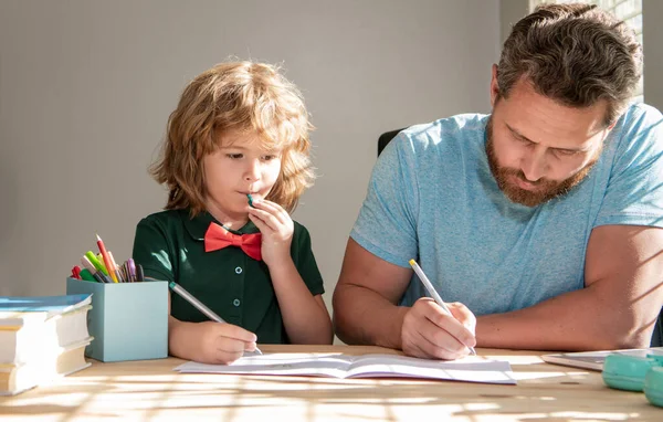 bearded father writing school homework with his boy son in classroom, school.