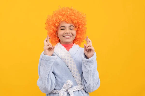 dreamy kid in fancy orange wig hair wear home bathrobe making wish, crossed finger.