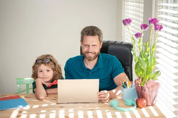 bearded dad or school private tutor teaching boy son with modern laptop, education.