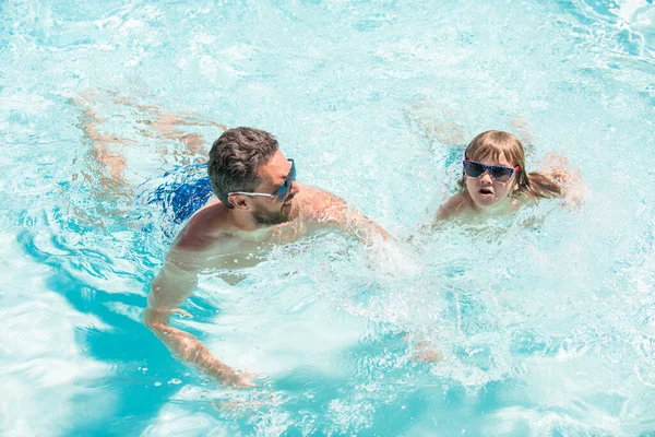 happy daddy with kid boy on spa resort. summer holidays weekend at family day. dad and child having fun at pool party. childhood and parenting. father and son wear glasses in swimming pool water.