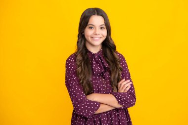 Sevimli küçük kız sarı arka planda kollarını kavuşturuyor.