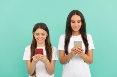 Mutlu anne ve kız mavi arka planda akıllı telefondan sohbet ediyorlar..
