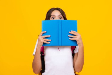 School teenage girl with school bag backpack hold book on yellow isolated studio background. Children school and education concept