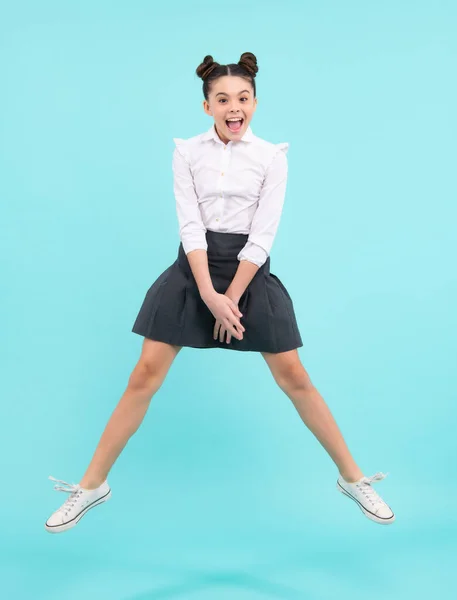 Excited face. Full length cheerful teenager kid jump enjoy rejoice win isolated on blue background. Small child girl in summer dress jumping.Amazed expression, cheerful and glad