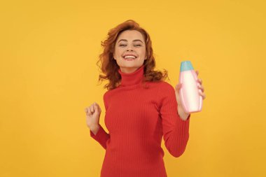 Kıvırcık saçlı kız şampuan şişesi sunuyor. Saç kremi reklamı. Güzellik ürünü. Günlük alışkanlıklar ve kişisel bakım. Kızıl saçlı kadın kozmetik ürünleri sunuyor. Mutlu kadın duş jeli kullan..