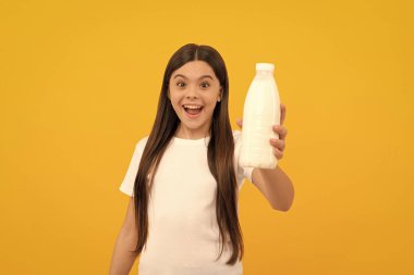 Şaşırmış çocuk süt ürünleri sunuyor. Genç kız süt içecek. Sağlıklı bir yaşam tarzı. Çocukluk gıdası. Günde bir içki. Süt ürünleri. Kahvaltıda yoğurt. Çocuk süt şişesini tutuyor..