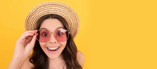 surprised kid in summer straw hat and glasses has curly hair on yellow background, summer sales. Child face, horizontal poster, teenager girl isolated portrait, banner with copy space