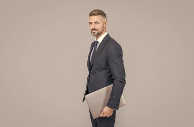 Resmi takım elbiseli, gri saçlı olgun bir ofis çalışanı. Bilgisayarı var, çevik iş yapıyor..