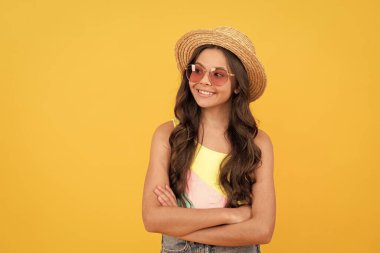 Yazın hasır şapkalı ve gözlüklü mutlu çocuk sarı arka planda kıvırcık saçlı, yaz.