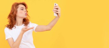 Kadın cep telefonunun sarı arka planına el öpme hareketi yapıyor, selfie. İzole edilmiş yüz portresi, taklit alanı olan pankart