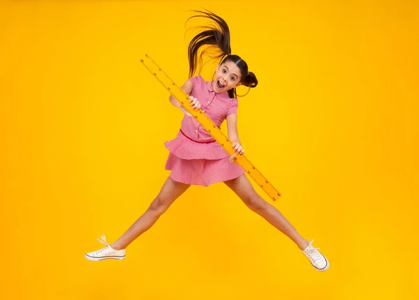 Amazed teenager. Back to school. School girl hold ruler measuring isolated on yellow background. Crazy jump, jumping kids. Excited teen schoolgirl