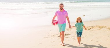 Baba ve oğul plajda futbol ya da futbol oynuyor. Mutlu baba ve oğul yaz plajında top ve aileyle yürür..