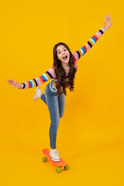 Teenagers lifestyle, casual youth culture. Teen girl with skateboard over isolated yellow studio background. Cool modern teenager in stylish clothes. Happy teenager, positive and smiling
