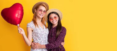 Mother and daughter kid banner, copy space, isolated background. happy mother and daughter hold love heart balloon on yellow background