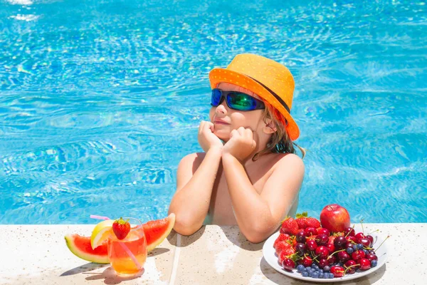 Little child by the pool eating fruit and drinking lemonade cocktail. Summer kids vacation concept