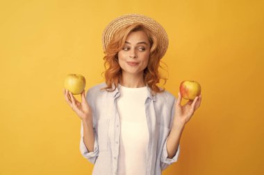 Gülümseyen, kıvırcık saçlı, yaz şapkalı, elmalı, vitaminli genç bir kadın..