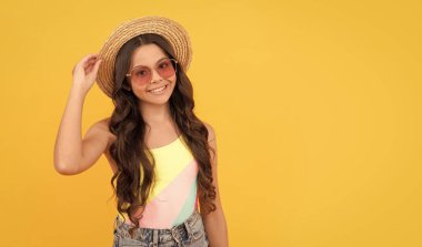 Gülümseyen çocuk hasır şapka ve gözlük takıyor. Sarı arka planda neşeli küçük bir kız. Mutlu çocuklar günü. Çocuk yaz modası. Plaj partisi. Sonunda yaz tatili. kopyalama alanı. küçük güzellik.