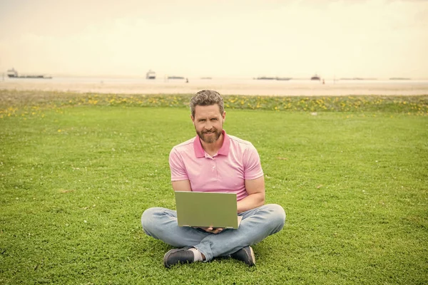 happy guy check email on computer relaxing on grass, modern life.