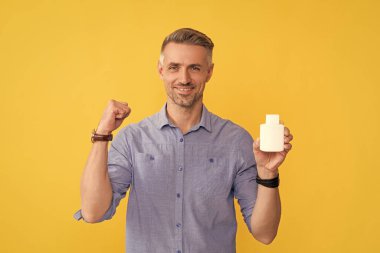 Mutlu adam sarı arka planda vitamin şişesi gösteriyor..
