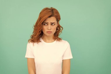 Mavi arka planda kıvırcık saçlı, üzgün, kızıl saçlı kadın..