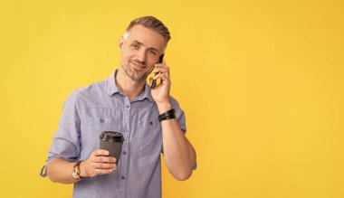 Gülümseyen yakışıklı adam kahve fincanıyla akıllı telefon kullanıyor. Kahve içen bir adam. Modern hayat ve yaşam tarzı. Adam paket çay içiyor. Günaydın. İletişim. Boşluğu kopyala.