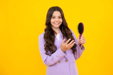 Sarı izole edilmiş stüdyo arka planında saçlarını tarayan bir genç. Saç fırçası olan genç bir kız. Çocukların saç stili. Genç kızın mutlu ve gülümseyen duyguları